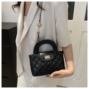 Détail d'un sac à main matelassé noir avec fermoir doré et boule ornée sur la bandoulière