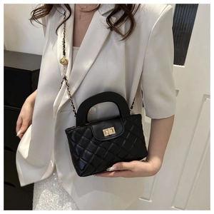 Detail of black quilted leather handbag with gold twist lock and chain strap on model