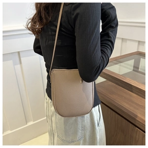 Detail of taupe litchi leather mini crossbody bucket bag worn by model in a chic setting