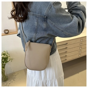Close-up of minimalist beige crossbody bag with lychee texture on casual outfit