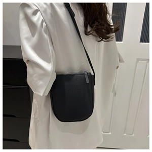 Detail of black pebbled leather crossbody bag with curved bottom on white suit model