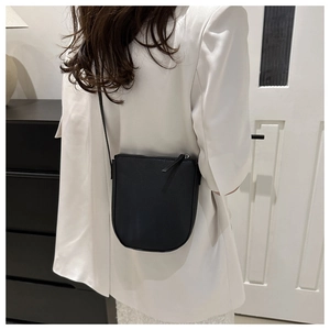 Rear view of a minimalist black pebble leather crossbody bag on a model wearing a white suit