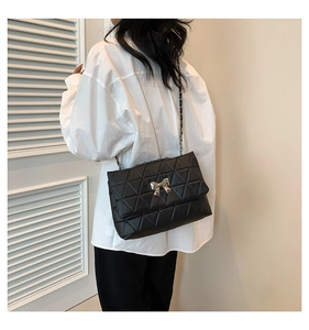 Close-up of black quilted shoulder bag with golden bow clasp and metal chain strap