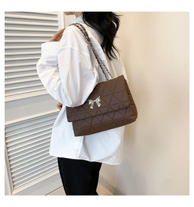 Detail of brown quilted PU leather crossbody bag with silver metal bow and chain strap