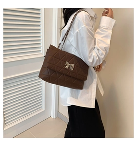 Close-up of coffee brown quilted shoulder bag with golden bow buckle and chain strap