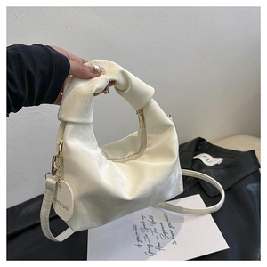 Detail of off-white ruched handbag with knotted handle and fashion tags on black coat