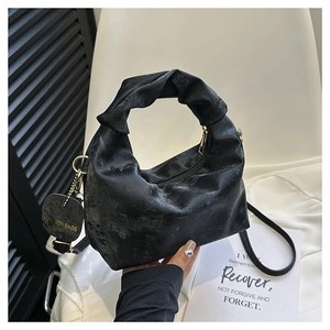 Detail of black ruched handbag with knotted handle, gold zipper, and fashion tag charm