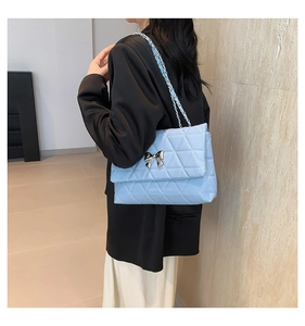 Detail of light blue quilted crossbody bag with silver bow accent on black blazer