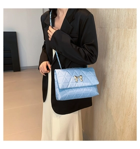 Detail of light blue quilted crossbody bag with gold bow clasp on a model outfit