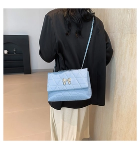 Detail of light blue quilted chain bag featuring a silver metal bow buckle on a model