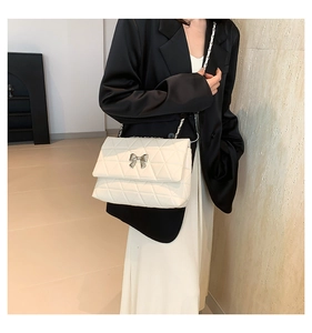 Detail of off-white quilted crossbody bag with silver bow buckle and chain strap