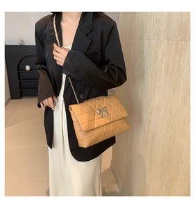 Detail of tan quilted crossbody bag with silver bow buckle and chain strap on model
