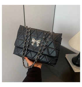 Detail of black quilted chain bag with silver bow clasp and woven metal strap