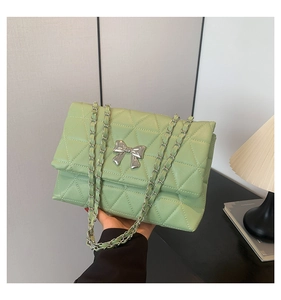 Close-up of light green quilted shoulder bag featuring silver bow and chain strap