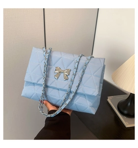 Detail of light blue quilted crossbody bag with silver bow buckle and chain strap