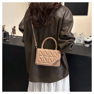 Détail d'un sac matelassé marron clair avec bordure métallique et poignée tissée au café