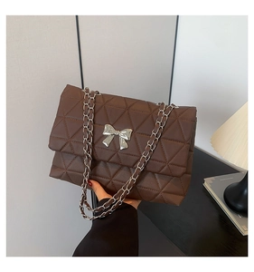 Detail of a brown quilted chain bag with a silver metal bow accent in a lifestyle setting