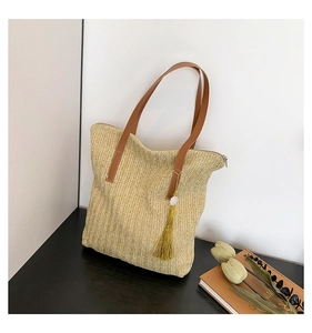 Détails d'un sac cabas en paille tressée avec anses en cuir et pompon décoratif jaune