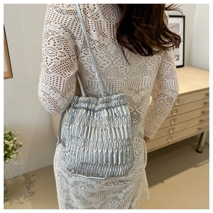 Detail of silver pleated drawstring bucket bag shown on model in a white lace dress