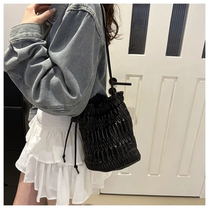 Detail of black drawstring bucket bag featuring soft pleated texture and slim shoulder strap