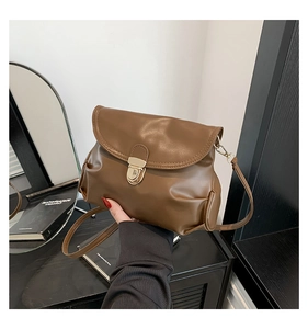 Close-up of brown pleated leather shoulder bag with gold metal buckle and soft texture