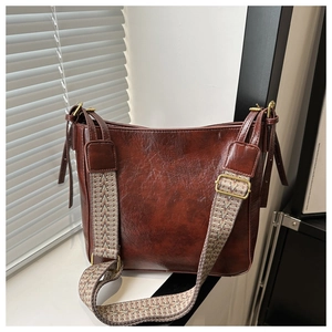 Détail d'un sac seau en cuir marron avec une bandoulière tissée aux motifs ethniques