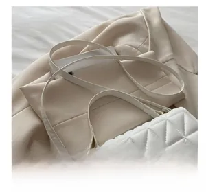 Detail of white quilted crossbody bag with golden metal trim on a beige blazer