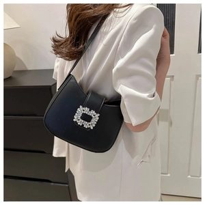 Détail du sac hobo noir avec boucle en strass porté sur un blazer blanc élégant
