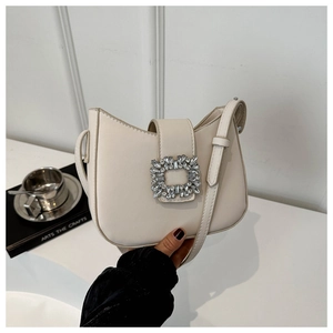 Détail du sac selle crème avec une boucle carrée ornée de strass brillants et élégants