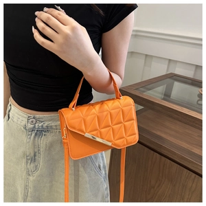 Close-up of orange quilted crossbody bag with gold metal bar and long shoulder strap