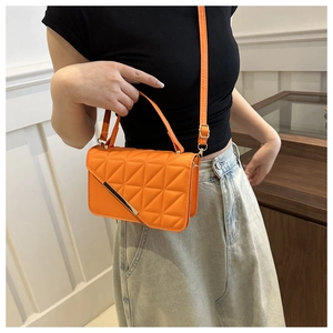 Detail of a bright orange quilted crossbody bag with a modern gold metal strip on the flap