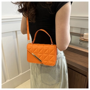 Side view of a bright orange quilted leather crossbody bag with gold metal accents