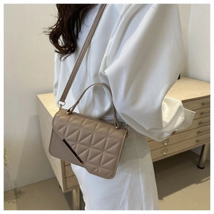 Detail of beige quilted handbag featuring elegant metal bar and adjustable shoulder strap
