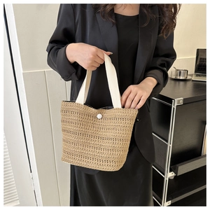 Détail d'un sac seau tissé montrant la bandoulière blanche et le bouton fermoir