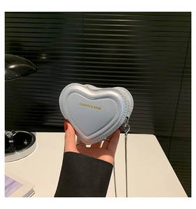 Detail of light blue heart-shaped bag featuring gold fashion lettering and silver chain strap