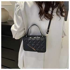 Detail view of black quilted crossbody bag with gold metal trim on model