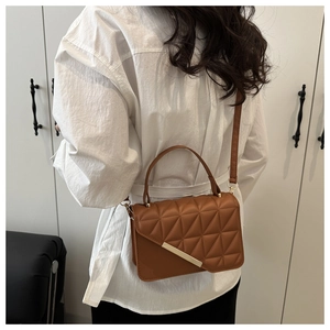 Close-up of brown quilted crossbody bag with gold metal trim worn by model