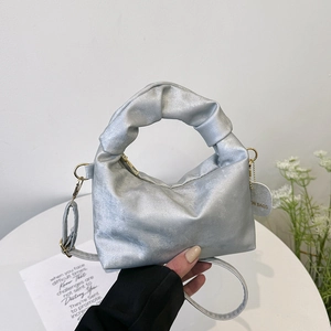 Silver metallic pleated handbag with ruffled handle and detachable strap in hand