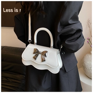 Détail d'un sac à main blanc aux bords ondulés avec un nœud en métal argenté et bandoulière