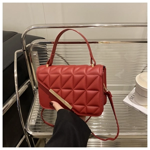Detailed view of red quilted leather handbag featuring a stylish gold diagonal metal bar