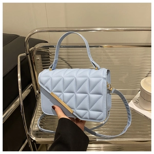 Detail of light blue quilted crossbody bag featuring elegant gold metal trim and top handle