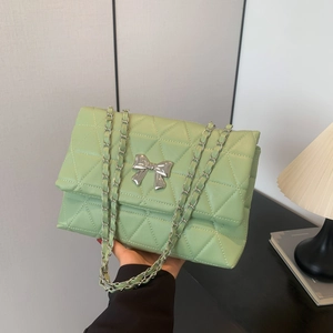 Chic green quilted shoulder bag with silver bow and chain strap held by a model