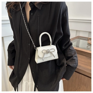 Gros plan d'un mini sac blanc avec un nœud en diamant étincelant et chaîne argentée