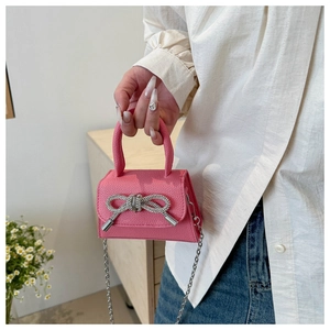 Détail d'un mini sac rose en cuir avec nœud strassé et fine chaîne argentée