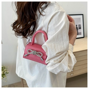Détail d'un sac à main rose en cuir grainé avec nœud en strass et chaîne argentée