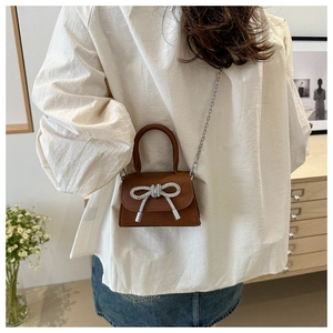 Mini sac bandoulière marron avec nœud en strass et chaîne argentée porté par un mannequin