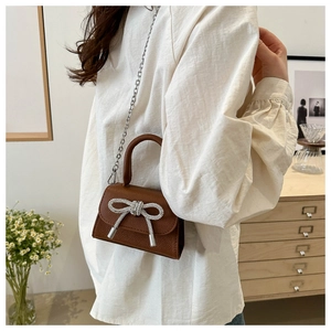 Détail d'un sac à main en cuir marron avec un nœud décoratif orné de strass argentés