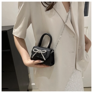 Détail du mini sac noir en cuir grainé avec un nœud élégant orné de strass brillants