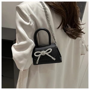 Détail du sac à bandoulière noir avec nœud en strass porté par un mannequin en blazer