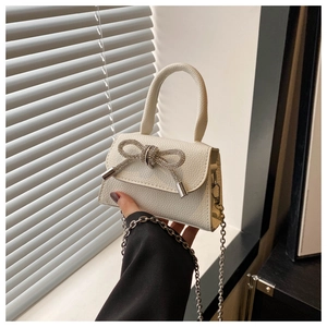 Gros plan d'un mini sac blanc en cuir avec un nœud en strass brillant et une chaîne argentée